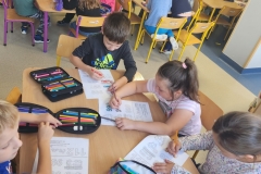 Kilkoro dzieci siedzi przy stoliku i maluje kredkami.