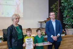 Dwóch chłopców w zielonych koszulkach stoi obok siebie. Po bokach stoi pan i pani.