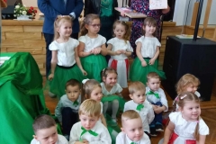 Dziesięcioro dzieci kuca na podłodze,  czworo  stoi. Za nimi stoją dwie panie i jeden  pan.