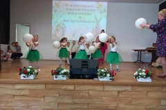 Grupa dziewczynek ubrana w białe  bluzeczki i zielone spódniczki trzymają w rękach  białe  balony.