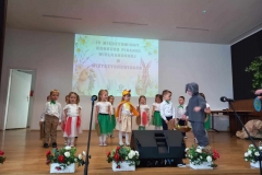 Dzieci stoją na scenie w dwuszeregu. Przed nimi dziecko ubrane w szary strój zajączka.