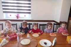 Pięcioro dzieci siedzi przy stoliku.  Przed nimi leżą okrągłe placki.