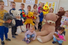 Grupa dzieci z wychowawczynią stoi w półkolu, każdy trzyma misia w ręku, największy leży na podłodze.