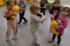 Grupa dzieci porusza się po obwodzie koła z przytulonymi do siebie misiami- tańczy. Za dziećmi stoliki i szafki z kącika kuchennego.