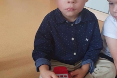 Chłopiec w granatowej koszuli w białe kropki trzyma w rękach czerwony telefon.