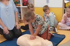 Chłopiec klęczy nad manekinem obok kobiety w niebieskiej bluzce i uciskanie jego klatkę piersiową.