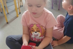 Dziewczynka w różowej bluzce z pieskiem trzyma czerwony telefon.