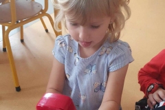 Blond dziewczynka w niebieskiej bluzce w motyle naciska przyciski na czerwonym telefonie.