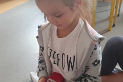 Dziewczynka w białym podkoszulku i bluzie trzyma czerwony telefon i wybiera numer.