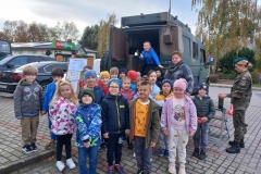 Dzieci wraz z wychowawczynią stoją przed samochodem wojskowym