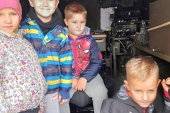 Czworo dzieci znajduje się wewnątrz samochodu  wojskowego. W tle widać różne urządzenia, które stanowią wyposażenie auta.