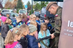 Grupa dzieci skupiona wokół żołnierza, który pokazuje im broń.