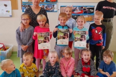 Grupa dzieci stoi, kilkoro siedzi na podłodze, troje dzieci trzyma w rękach certyfikaty I dyplom.