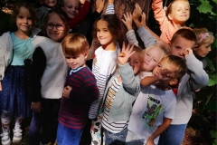 Grupa dzieci przytula się do drzewa w lesie.