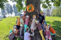 Grupa dzieci ubranych w kolorowe stroje przytula się do drzewa.