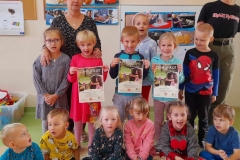 Grupa dzieci stroi. Kilkoro siedzi na podłodze, troje dzieci trzyma w ręce certyfikaty i dyplom.