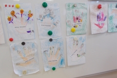 Na białej tablicy przypięte są małe pokolorowane kartki. Na każdej odrysowana jest dłoń dziecka, na palcach narysowano postacie członków rodziny. Każda dłoń ma napis : Moja rodzina.