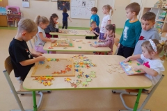 Dzieci siedzą po obu stronach stolika, układają puzzle. Wiesława Wiesława Troje dzieci układa puzzle przy stolikach. Wiesława Wiesława Czworo dzieci stoi, w ręku trzymają medale za zajęcie pierwszego miejsca w konkursie układania puzzli. Wiesława Wiesława Piecioro dzieci stoi obok siebie, w ręku trzymają medale za zajęcie drugiego miejsca w konkursie układania puzzli. Wiesława Wiesława Dwóch chłopców stoi obok siebie  w ręku trzymają medale za zajęcie trzeciego miejsca w konkursie układania puzzli. Wiesława Wiesława Patoń Wiesława Wiesława Patoń Konkurs układania puzzli u Misiów. W piątek wśród Misiów odbył się konkurs układania puzzli. Jest to grupa mieszana dlatego, stopień trudności był zróżnicowany. Dzieci młodsze układały łatwiejsze puzzle, starsze trudniejsze z większą ilością elementów. Podczas konkursu wyrabiano u dzieci umiejętność logicznego myślenia i koncentracji, słuchania poleceń nauczyciela oraz wdrażano je do zgodnej rywalizacji. W konkursie wzięło udział 11 dzieci. Czas minął nam miło i radośnie.