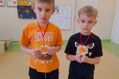 Dwóch chłopców stoi obok siebie  w ręku trzymają medale za zajęcie trzeciego miejsca w konkursie układania puzzli.