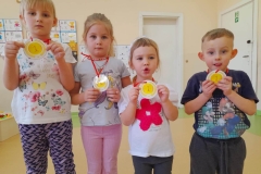 Czworo dzieci stoi, w ręku trzymają medale za zajęcie pierwszego miejsca w konkursie układania puzzli.