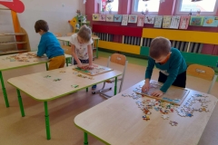 Troje dzieci układa puzzle przy stolikach.