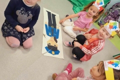 Cztery dziewczynki siedzą na podłodze.  Przed  nimi  leży z ułożonych puzzli postać policjanta.