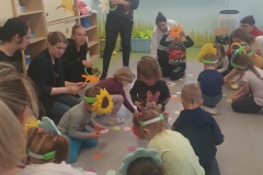 Dzieci wraz z rodzicami zbierają papierowe kwiatki z podłogi.