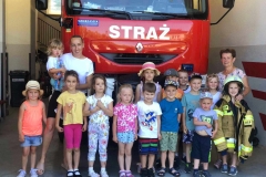 Grupa dzieci z wychowawcą stoi przed wozem strażackim, mama trzyma na rękach dziewczynkę.