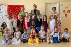  Grupa dzieci stoi w rzędzie, kilkoro siedzi na podłodze. Za nimi stoją zaproszeni goście i wychowawczyni.