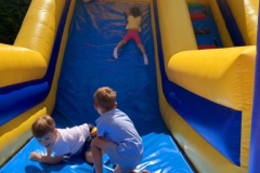 Trójka dzieci zjeżdża na kolorowym dmuchańcu.