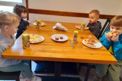 Dzieci siedzą przy stoliku  jedzą pizzę.