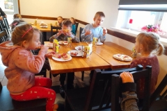 Dzieci siedzą przy stoliku  jedzą pizzę.