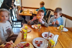 Dzieci siedzą przy stoliku  jedzą pizzę.