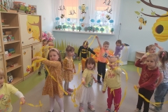 Dzieci w lużnej rozsypce tańczą do muzyki z żółtymi wstążkami.