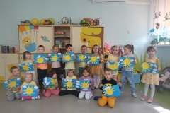 Grupa dzieci w przedszkolnej sali. Każde dziecko trzyma wyklejone słoneczko na niebieskim tle.