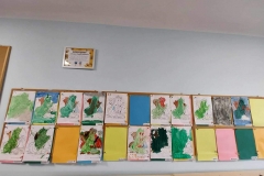 Na niebieskiej ścianie tablica korkowa. Na niej prace plastyczne dzieci- smok wawelski malowany farbami plakatowymi. Pod rysunkiem imię dziecka. Nad tablicą w białej ramce podziękowanie od dzieci za przyjęcie w szeregi przedszkola.