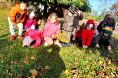 Grupa dzieci kuca pod ozdobnym drzewkiem.