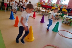 Dwóch chłopców dobiega do obręczy, w tle dwa rzędy dzieci i kolorowe pachołki ustawione w dwóch rzędach.