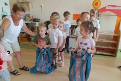 Dzieci stoją w dwóch rzędach, pierwsze dwie osoby przygotowują się do skoków w workach.