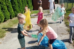 Na zdjęciu grup dzieci z dwoma paniami, każde dzecko ma na ręce foliowe rękawiczki. Trójka dzieci trzyma kolorowe worki.