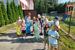 Na zdjęciu grup dzieci z dwoma paniami, każde dzecko ma na ręce foliowe rękawiczki. Trójka dzieci trzyma kolorowe worki.