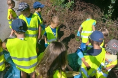 Dzieci w odblaskowych kamizelkach zbierają śmieci.