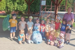 Czworo dzieci kuca w pierwszym rzędzie, za nimi stoi 10 przedszkolaków, obok nich pani. Są też worki z zebranymi śmieciami.