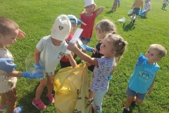 Dzieci ubrane w kolorowe stroje wrzucają do żółtego worka zebrane papiery.