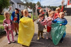 Grupa dzieci zbiera śmieci przed garażem. Na pierwszym planie dziewczynka trzyma w ręce żółty worek. W tle chłopiec wrzuca papier do niebieskiego worka.