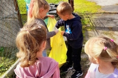 Na zdjęciu trzy dziewczynki, jedna z nich trzyma żółty worek do którego chłopiec wrzuca butelkę. W tle chłopiec z zielonym workiem.