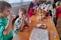 Dzieci siedzą z seniorami przy stolikach, częstują się słodyczami.