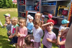 Dzieci w kolorowych strojach stoją na tle wozu strażackiego.