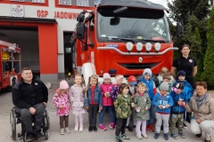 Grupa dzieci stoi przed wozem strażackim z druhem Marcinem oraz druhną Julią.