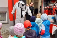 Druhną Julią pokazuje dzieciom skafander strażacki.